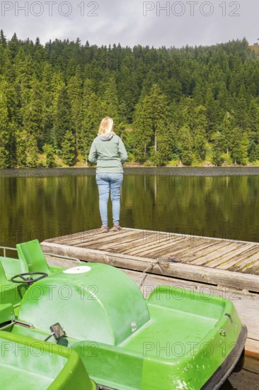 A person stands on a footbridge, looking at a quiet lake in the forest, Mummelsee, Seebach, Ortenau