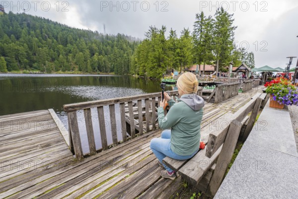 Woman at the lake photographed with her smartphone from a wooden jetty, Mummelsee, Seebach, Ortenau