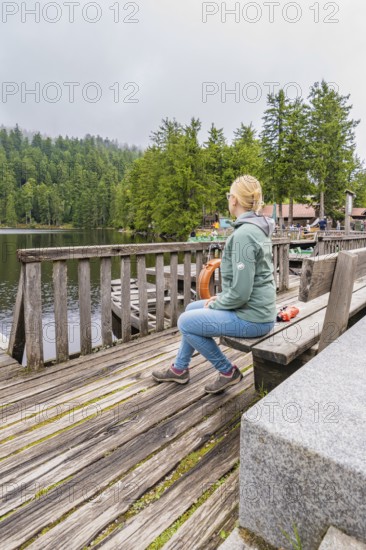 A woman sits relaxed on a wooden bench overlooking the tranquil lake and forest, Mummelsee,