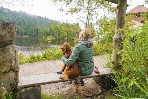 Woman with dog on a bench by the lake in the countryside, relaxed atmosphere in nature, Mummelsee,