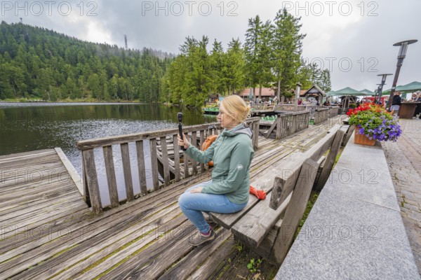Woman on a wooden footbridge next to a lake with a camera in her hand, Mummelsee, Seebach, Ortenau