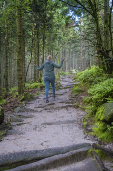 Woman walking along a forest path, surrounded by trees and moss, joyful movement, Mummelsee,