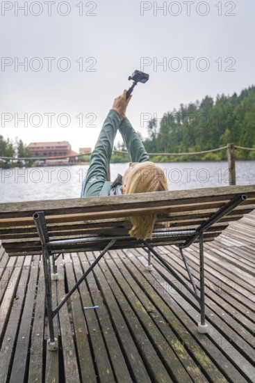 Woman lying on a bench by the lake and holding a camera, Mummelsee, Seebach, Ortenau district,