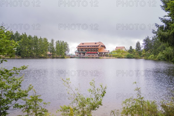 A hotel on the shore of a lake, surrounded by forest and overcast skies, Mummelsee, Seebach,