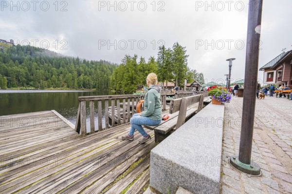 Woman on a bench next to a lake and flowers on a wooden footbridge, Mummelsee, Seebach, Ortenau