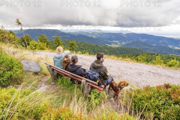 Group on a bench marvelling at the panorama over the mountain landscape with clouds in the sky,
