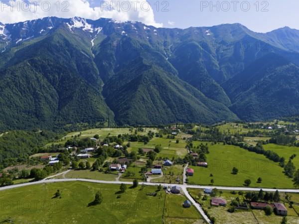 A small village in the middle of a vast green landscape with high mountains in the background,