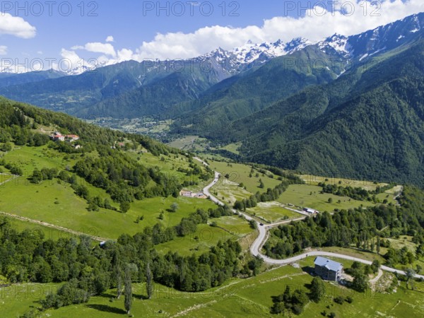 Panoramic view of a valley with roads and forests, surrounded by mountains under a clear sky,