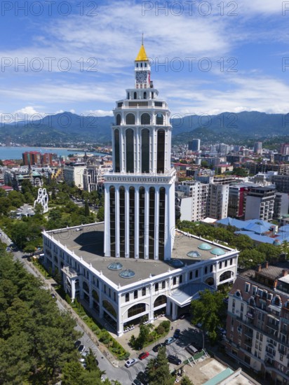 A tall modern building in an urban environment with mountains, aerial view, Sheraton Hotel, Batumi,
