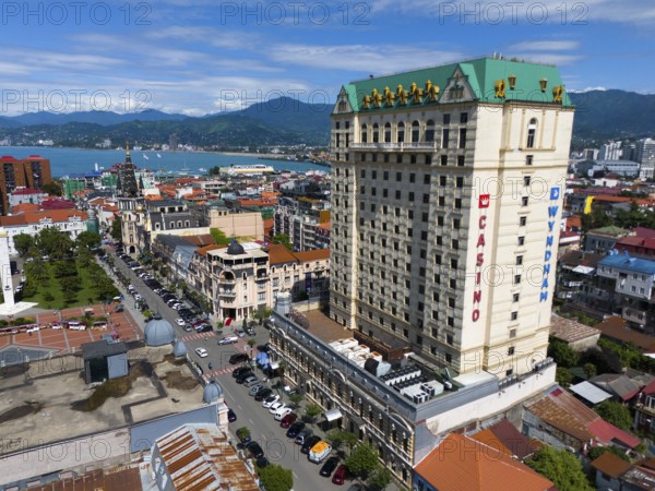 Large hotel building in a coastal town with mountains in the background and lively street scene,