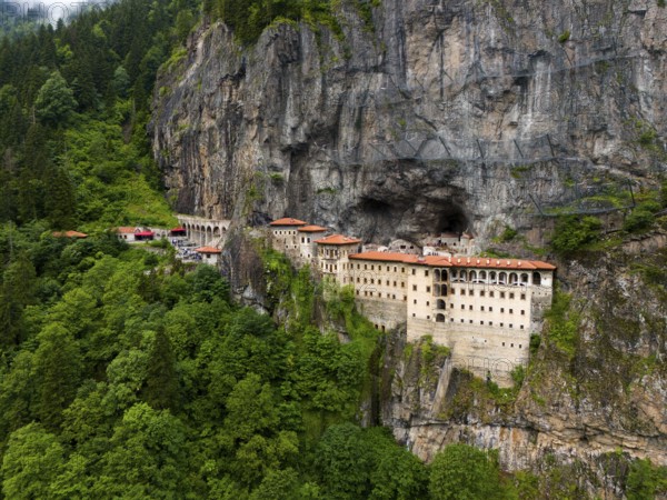 A monastery embedded in a green rocky landscape surrounded by dense forest, aerial view, Sumela