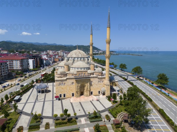 Panoramic view of a large mosque with minarets on a coastline flanked by streets and buildings,
