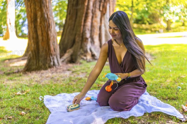 Latin mom arranging colorful baby toys on blanket in park, enjoying quality time with her child in