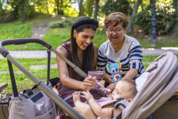 Grandmother, mother and baby girl enjoying time together at the park, feeding the baby girl and