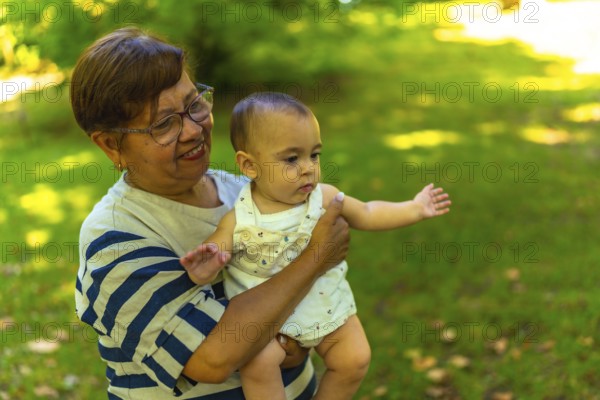 Smiling grandmother cradling her adorable granddaughter in a vibrant green park, enjoying a sunny