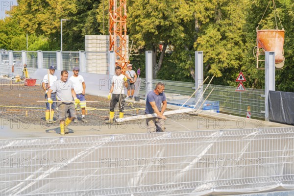 Group of construction workers on a building site with warning signs and a crane nearby, car park