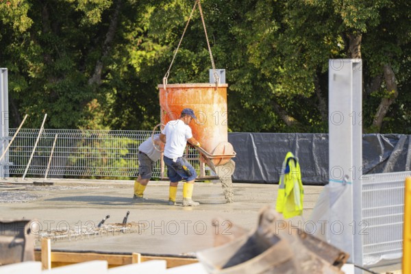 Construction workers pouring concrete from a concrete mixer on a building site with lattice fence