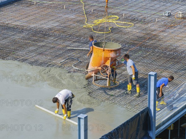 Workers pouring concrete on a construction site with concrete mixer and steel frame structure in