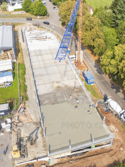 Top view of a construction site with crane and workers, surrounded by trees and roads, car park