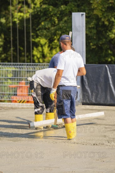 Close-up of construction workers concreting on a building site with safety equipment, car park