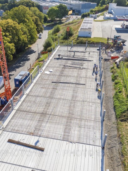 Workers on construction site with crane in sunny weather, surrounded by roads and fences, car park