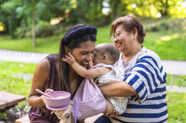 Latin family enjoying time together in park, grandmother holding granddaughter while mother is
