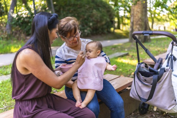 Latin family enjoying a sunny day outdoors, with grandmother and mother lovingly feeding a baby