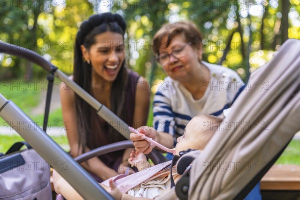 Grandmother feeds baby girl sitting in stroller, while mother watches, enjoying family time