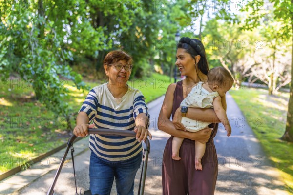 Grandmother, mother, and baby girl enjoying a sunny day at the park, pushing a stroller and