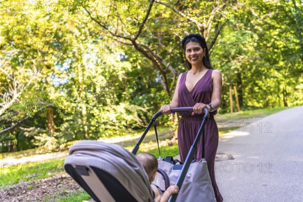 Latin mother enjoying a sunny summer day while walking in the park with her baby in a stroller,