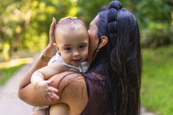 Mother cuddling her baby girl while strolling through a park, savoring a sunny day filled with