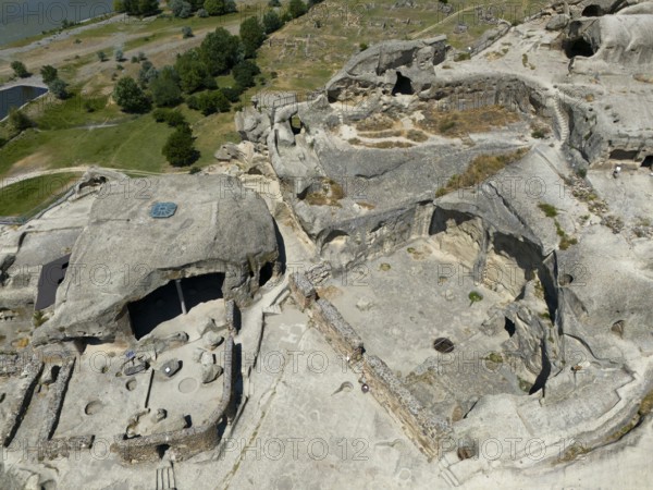 Cave complex with ruins near a river, surrounded by lush nature and rocks, aerial view, cave town