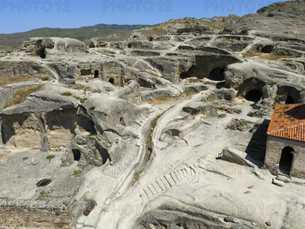 Ancient cave town with weathered sandstone structures and old paths under a blue sky, aerial view,