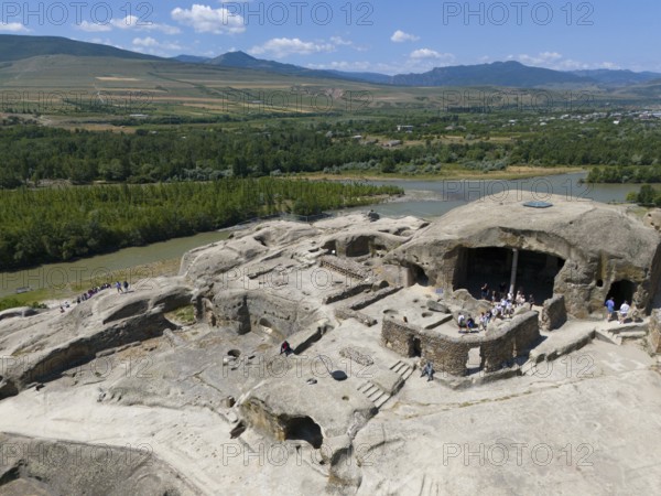 Ancient ruins with tourist visitors, surrounded by river landscapes and mountains, aerial view,