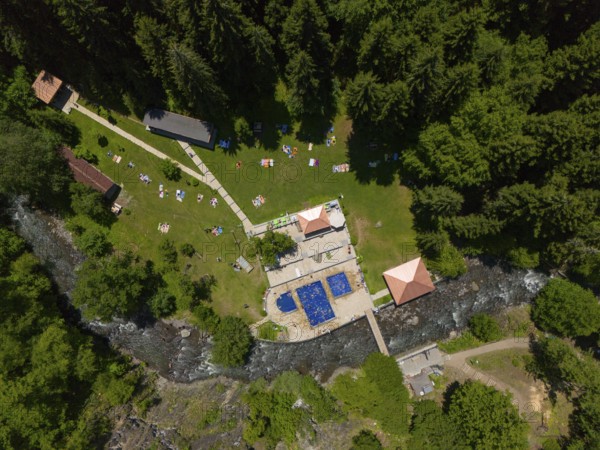 Aerial view of a forest area with swimming pool, river and surrounding buildings, surrounded by