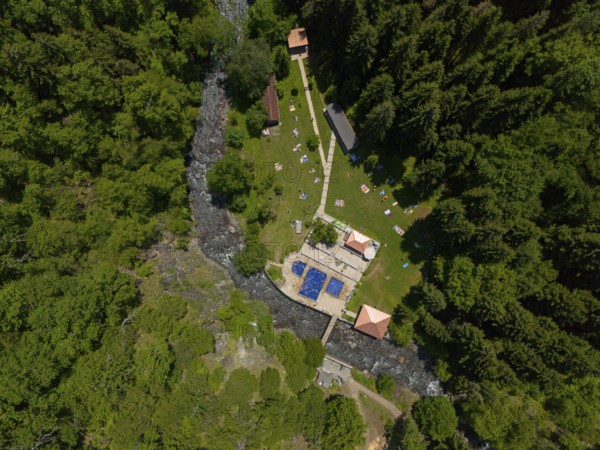 Aerial view of a forest area with swimming pool and river, surrounded by dense trees and buildings,