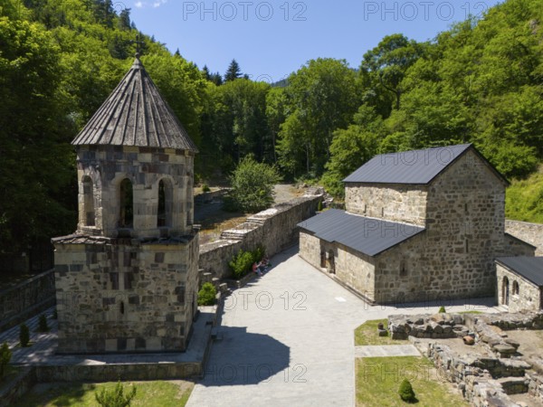 Stone chapel with adjoining buildings in a forest landscape under a clear blue sky, aerial view,