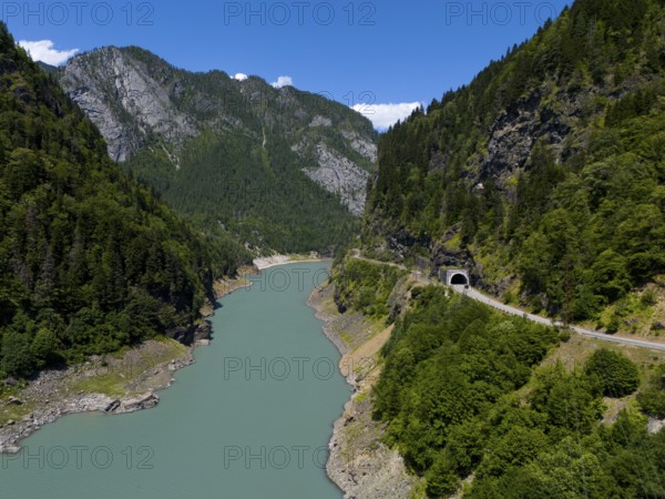 A turquoise-coloured river flows through a wooded valley with mountains and a tunnel in the