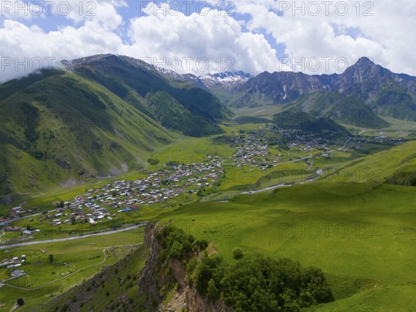 Panoramic view of green valley with village and mountains under a cloudy sky, aerial view, view