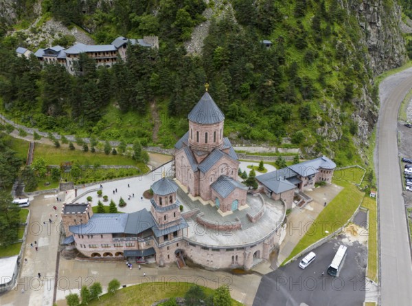 Large red brick church embedded in a wooded mountain landscape under a slightly cloudy sky, aerial
