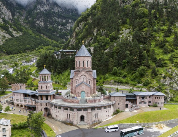 Impressive red brick church surrounded by forested mountains under a cloudy sky, aerial view,