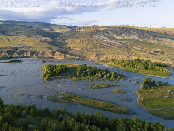 A picturesque river landscape with green islands and surrounding hills under a blue sky, aerial