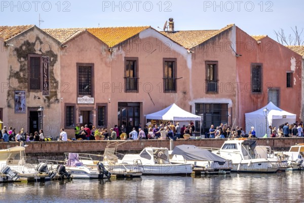 Sardinia, boats in the river Temo and houses on the promenade, guests at the restaurants with