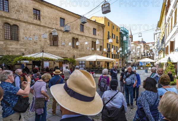 Sardinia, tourist tour group in the old town with sandstone-coloured palazzi, birdcage from house