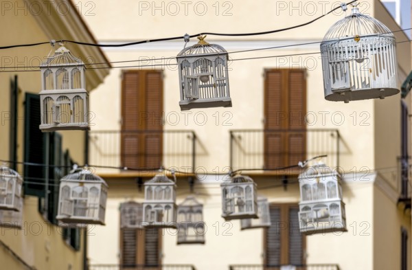 Sardinia, birdcage with light bulbs on power lines between houses above the street, old town,