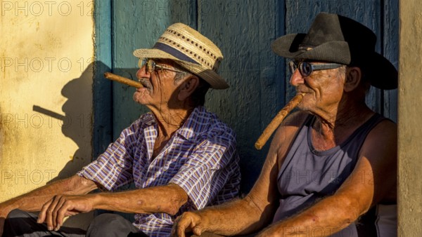 Two old Cubans smoking cigars and sitting on a staircase in the warm light of the sunset, Trinidad,