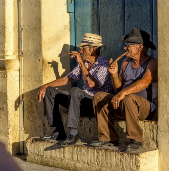 Two old Cubans smoking cigars and sitting on a staircase in the warm light of the sunset, Trinidad,