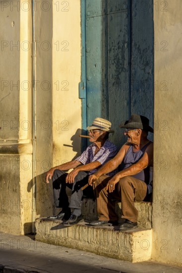 Two old Cubans smoking cigars and sitting on a staircase in the warm light of the sunset, Trinidad,