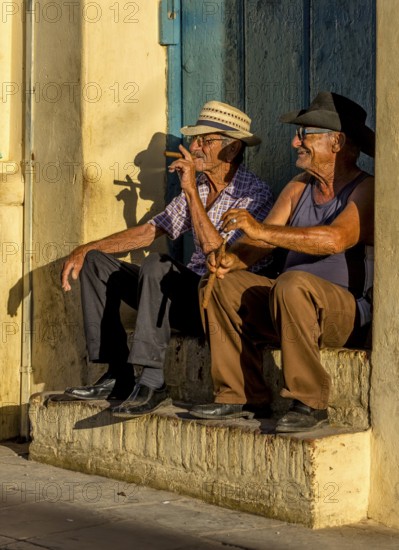 Two old Cubans smoking cigars and sitting on a staircase in the warm light of the sunset, Trinidad,
