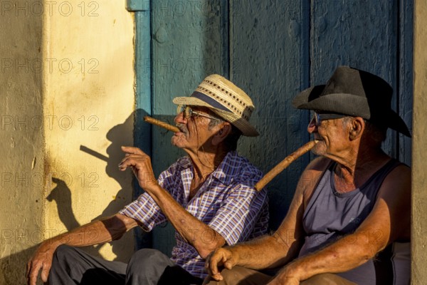 Two old Cubans smoking cigars and sitting on a staircase in the warm light of the sunset, Trinidad,